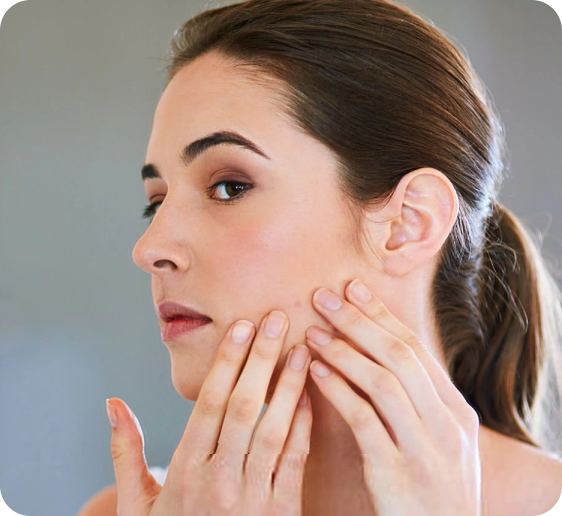 Woman in profile examining her cheek with her fingertips against a neutral background